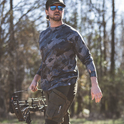 Man walking in woods wearing West Virginia State Camo Men's long sleeve shirt.