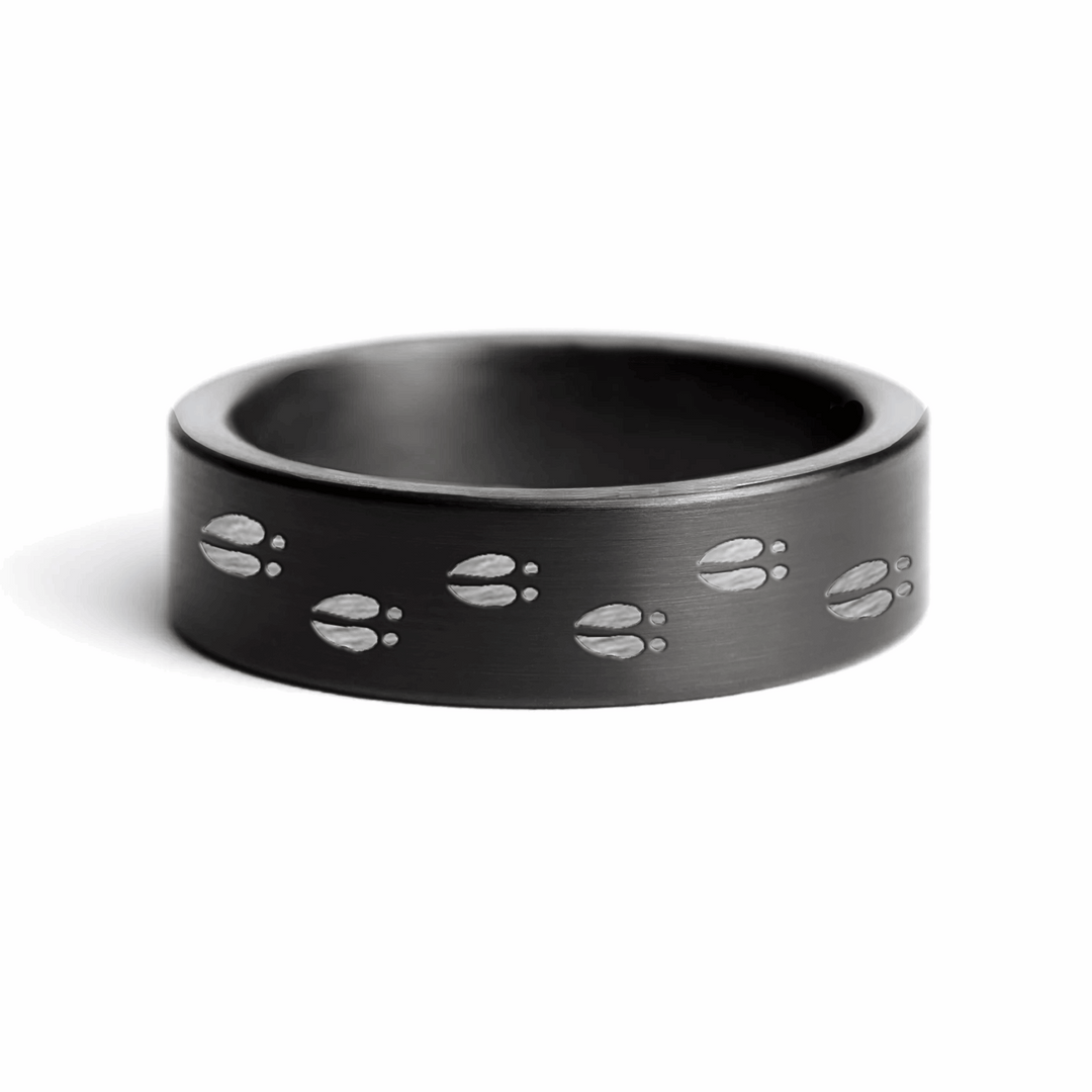 A black gunmetal ring with engraved white tail track pattern, cut from a steel shotgun barrel.
