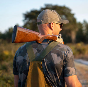Man in field with shotgun on shoulder wearing South Carolina State Camo short sleeve shirt