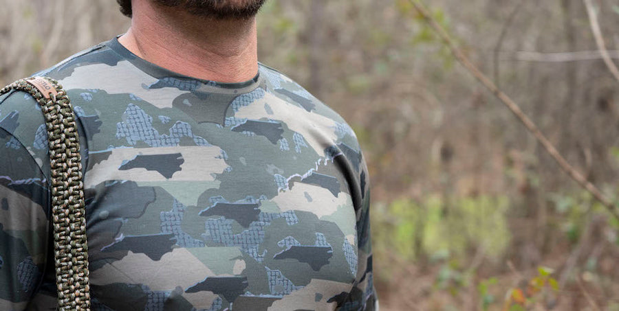 Man in woods with strap on his shoulder wearing North Carolina State Camo long sleeve shirt