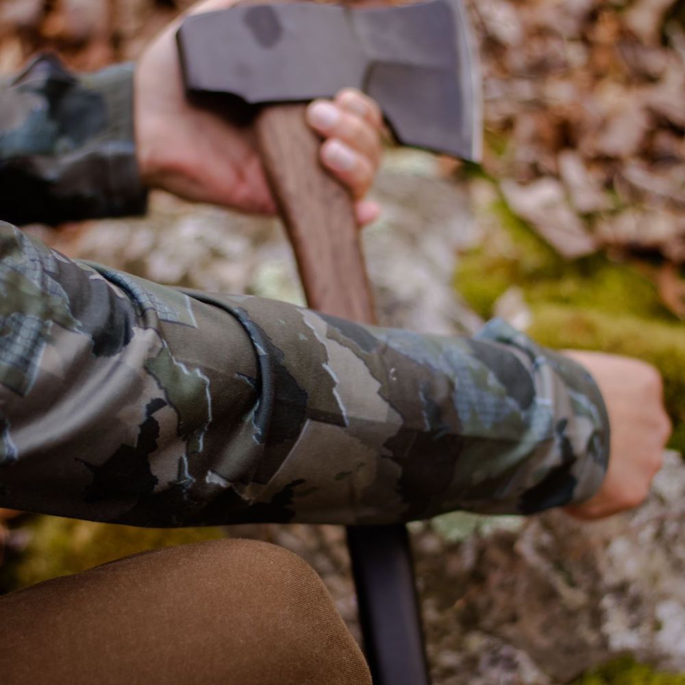 Man Holding axe Man walking in woods wearing West Virginia State Camo Men's long sleeve shirt.