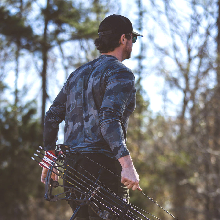 Man walking in woods wearing West Virginia State Camo Men's long sleeve shirt.